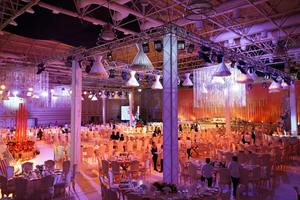 Large luxury wedding reception with dramatic overhead lighting rig, crystal chandeliers and elegant banquet tables set inside a transformed event space.