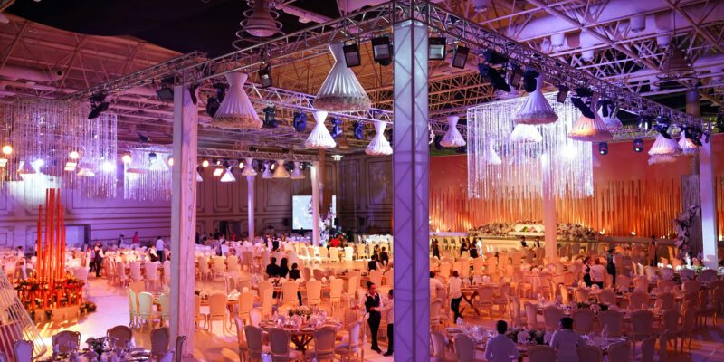 Large luxury wedding reception with dramatic overhead lighting rig, crystal chandeliers and elegant banquet tables set inside a transformed event space.