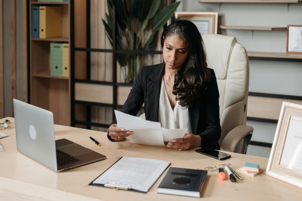 Professional woman reviewing paperwork at an office desk with a laptop, representing business compliance, legal administration and data protection processes.